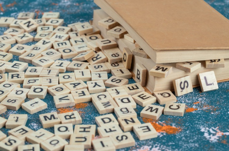 Peças de madeira com letras de madeira espalhadas sobre uma mesa e entre as páginas de um livro